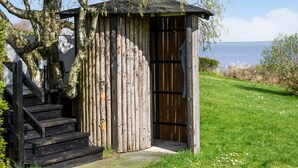 Une structure en bois dotée d’une porte et d’un escalier menant à l’entrée, située dans un espace verdoyant et offrant une vue sur la mer.