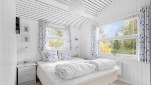 Une chambre à coucher avec un lit, une table de chevet, une lampe et une vue sur les arbres par la fenêtre.