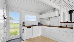 Une cuisine moderne avec des meubles blancs, un plan de travail en bois et une vue sur un paysage verdoyant, visible à travers une grande fenêtre.