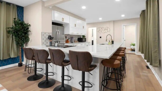 A modern kitchen with white cabinets, a central island with bar stools, and a visible sink. - Walk to OSU: Relaxing Retreat with Hot Tub (Columbus)