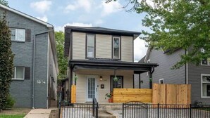 A two-story house with a front porch, a wooden fence, and a small garden area. - Walk to OSU: Relaxing Retreat with Hot Tub (Columbus)