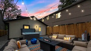 An outdoor living area with a fire pit, outdoor furniture, and string lights against a sunset sky. - Walk to OSU: Relaxing Retreat with Hot Tub (Columbus)