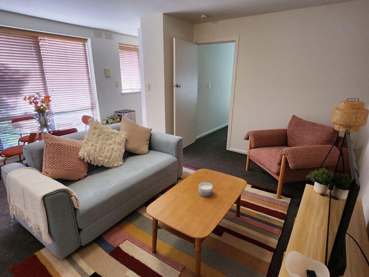 A living room with a grey sofa, a wooden coffee table, a pink armchair, and a striped rug.