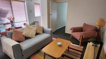A living room with a grey sofa, a wooden coffee table, a pink armchair, and a striped rug.