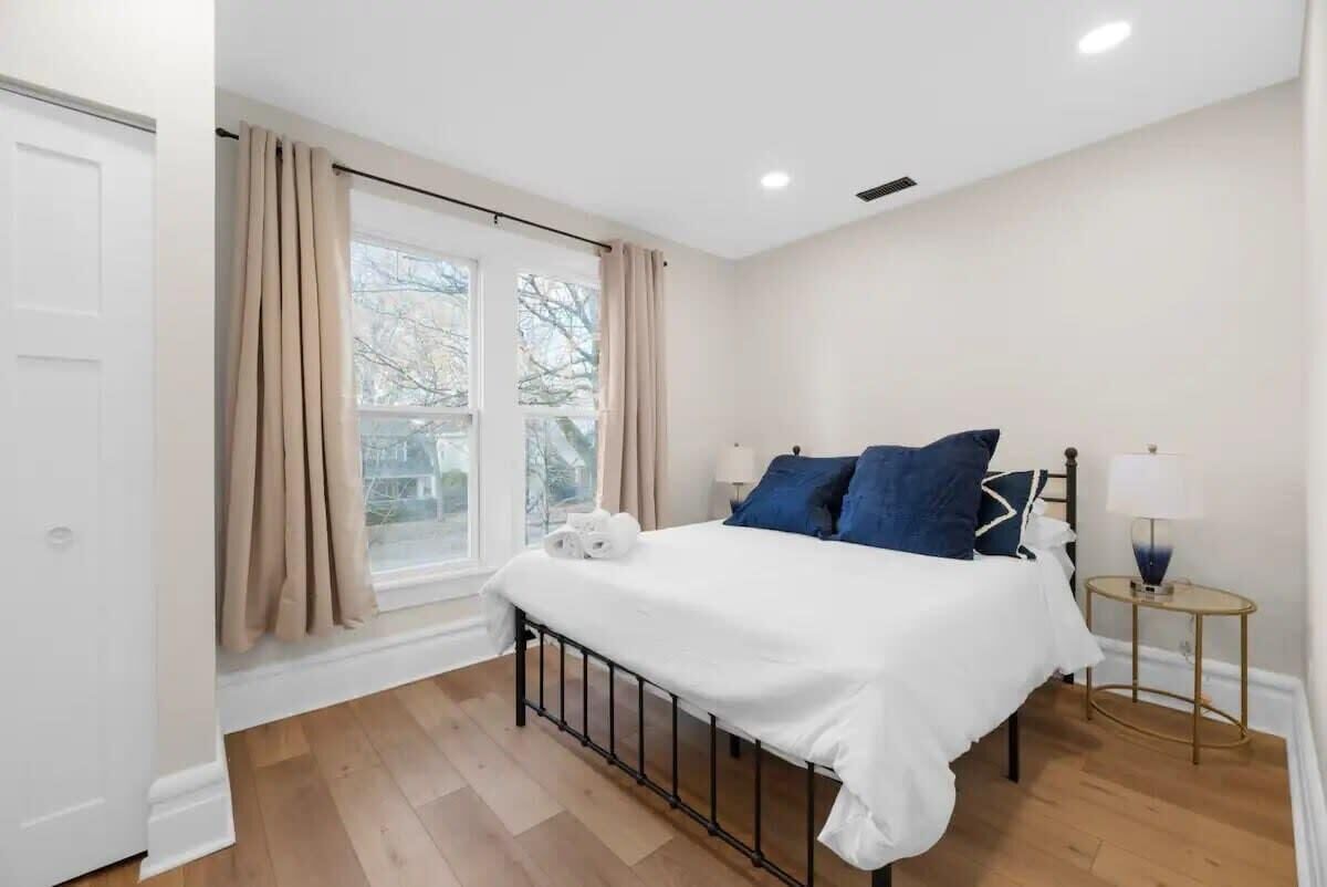A bedroom with a bed, a nightstand, a window with curtains, and a view of trees outside.