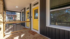 A covered porch with a wooden railing, a yellow door, and a large window. - Spacious 5-Bedroom Home with Hot Tub (Columbus)