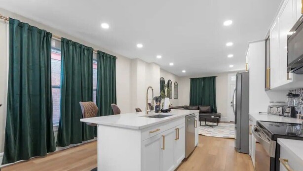 A modern kitchen with white cabinetry, a central island, and a dining area with a sofa and chairs. - Spacious 5-Bedroom Home with Hot Tub (Columbus)