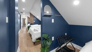 A hotel corridor with blue walls, a mirrored alcove, and a bed with a white cover. - Spacious 5-Bedroom Home with Hot Tub (Columbus)