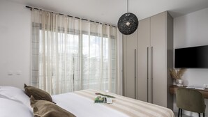Un dormitorio moderno con cama, cortinas, un escritorio, una silla y un televisor.