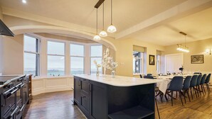 A spacious kitchen with a large island, wooden flooring, and large windows offering a view.