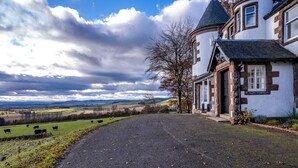 A countryside house with a paved driveway, a large field with cows, and a cloudy sky.