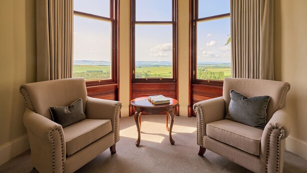 A room with two armchairs, a small table, and a bay window with a view of a green landscape.