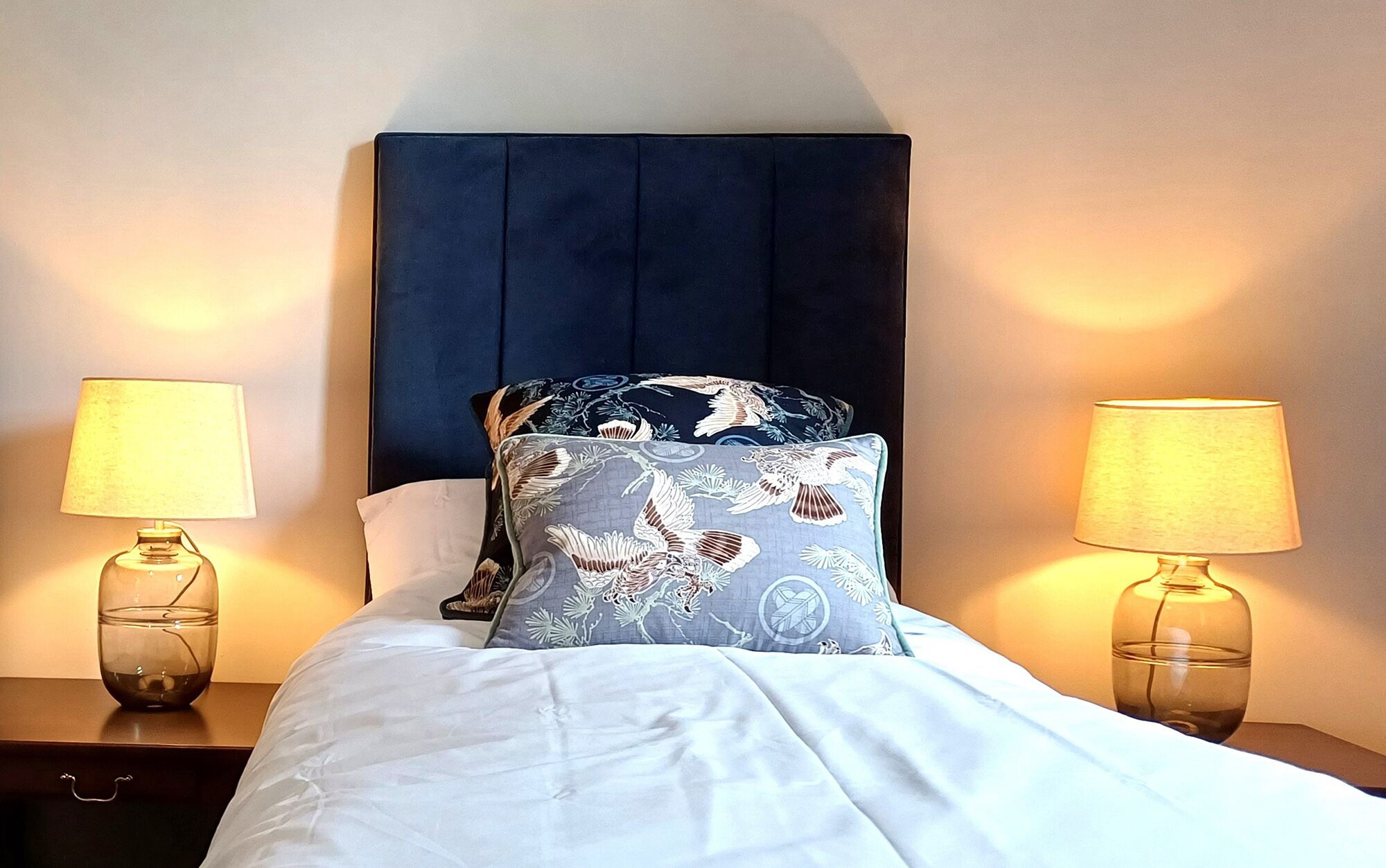 A neatly made bed with a dark headboard, two bedside lamps, and a floral pillow.
