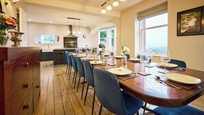 A dining area with a long wooden table set for a meal, blue chairs, and a view of the outdoors through large windows.