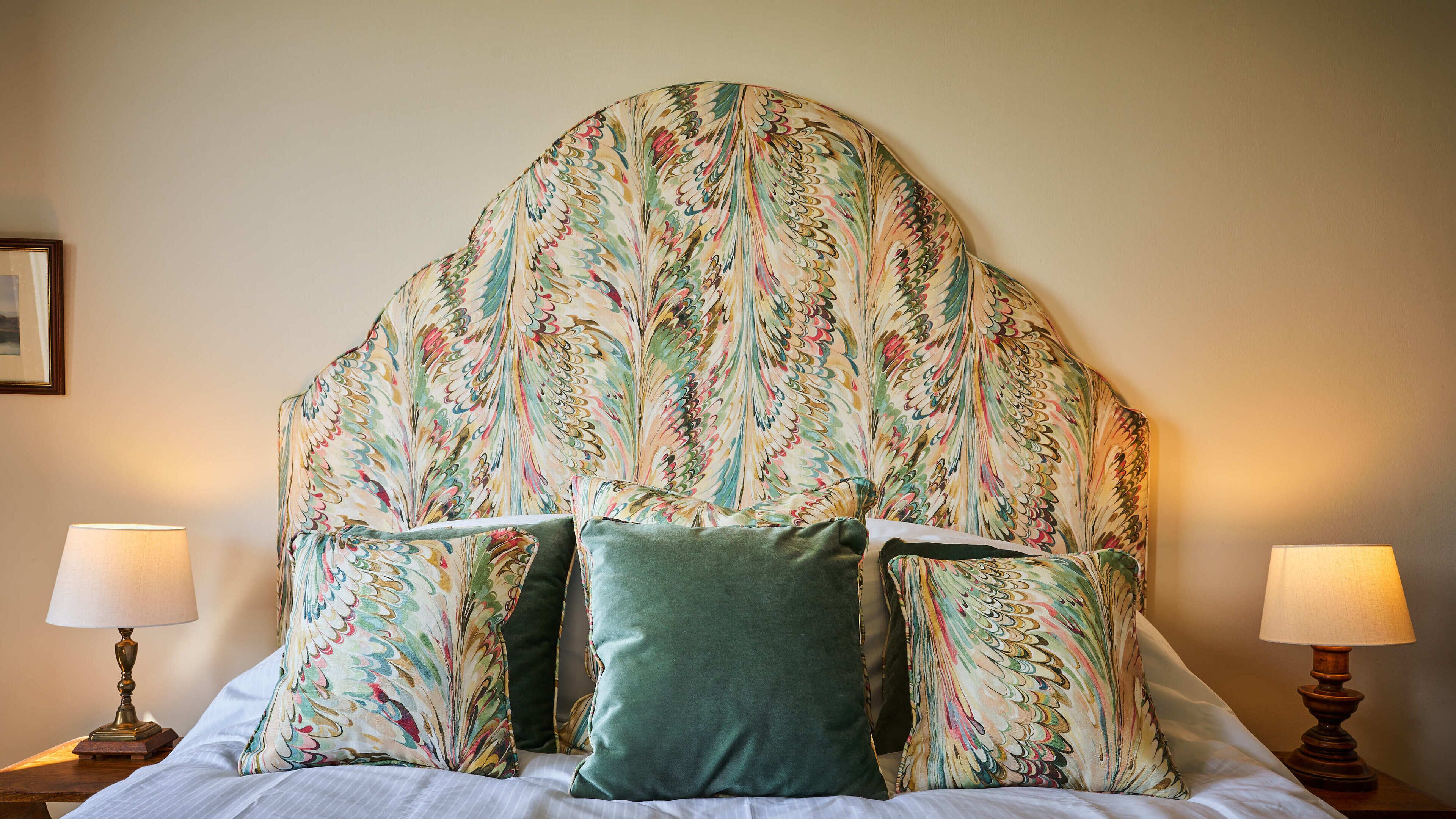 Ein Bett mit einem blumengemusterten Kopfteil, zwei Nachttischlampen und ein gerahmtes Bild an der Wand.