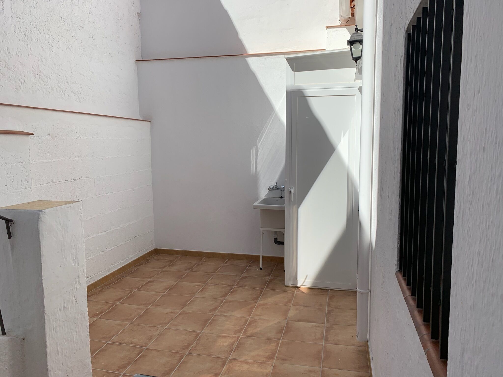 A small, enclosed bathroom with a white sink and a window with bars.