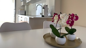 A modern kitchen with white cabinets, a stainless steel range hood, and a coffee maker on the counter. There is a dining table with a gold tray holding three white pots with green plants.