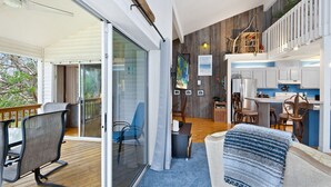 Un vaste espace de vie avec une porte-fenêtre coulissante donnant sur un balcon, une cuisine avec des meubles blancs et un coin repas avec des chaises bleues.