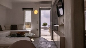 A modern hotel room with a minimalist design, featuring a sofa, a small table, and a view of the outdoors. - 2 Bedroom Villa with Private  Glass Pool & Shared Infinity Pool, Gym, Pool Bar (Mykonos)
