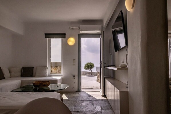 A modern hotel room with a minimalist design, featuring a sofa, a small table, and a view of the outdoors.