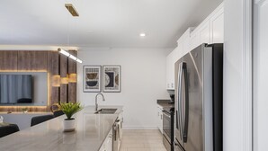 A modern kitchen with a large island, stainless steel appliances, and a flat-screen TV mounted above the island. - 4BR/3BA Townhome with private pool near Disney (Kissimmee)