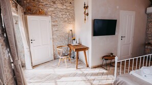 A room with a stone wall, a wooden table, a chair, a small side table, and a TV mounted on the wall.