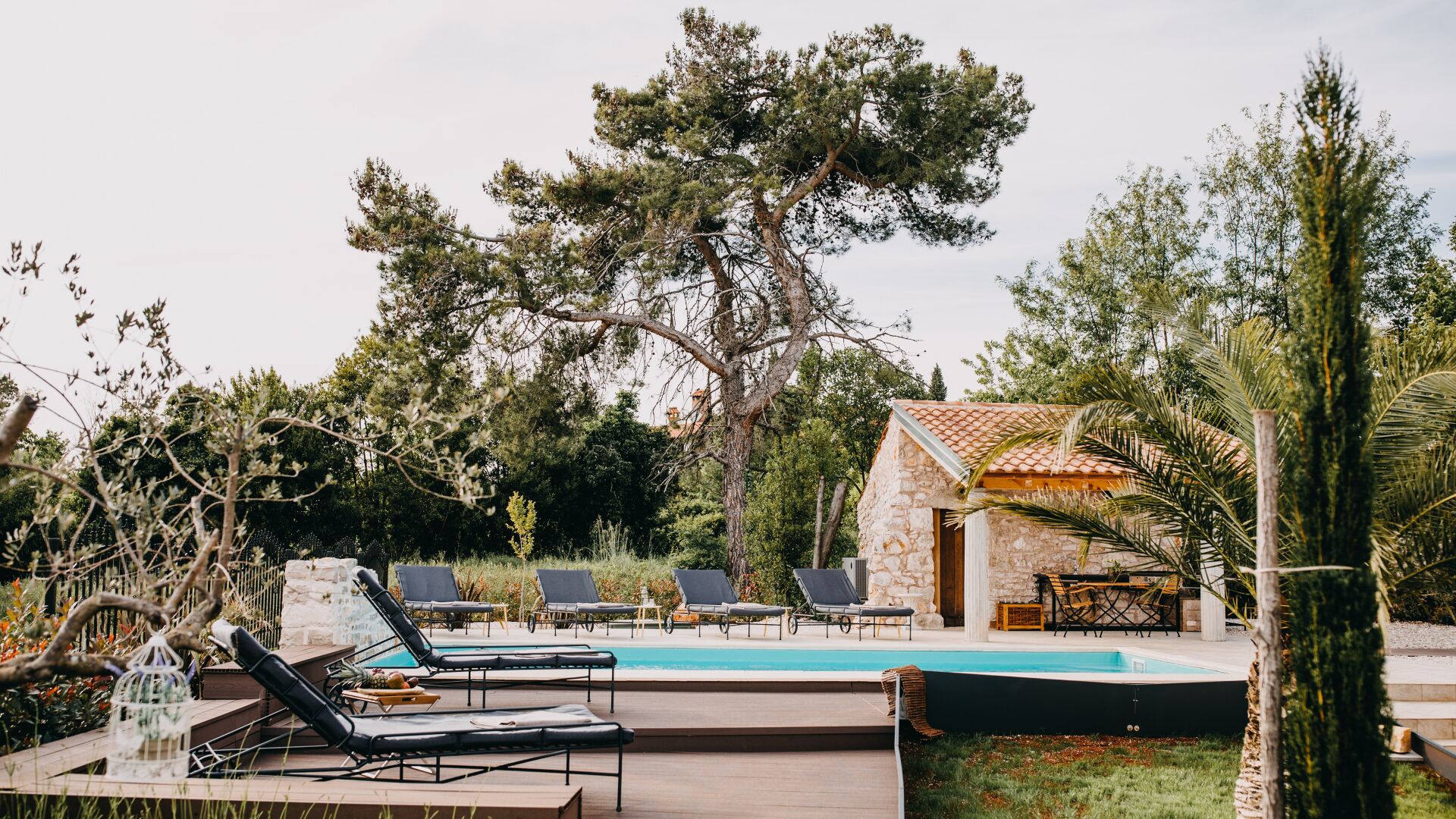 A pool area with lounge chairs, a stone building, and surrounding trees.