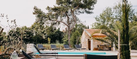 A pool area with lounge chairs, a stone building, and surrounding trees.
