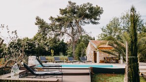 A pool area with lounge chairs, a stone building, and surrounding trees.