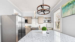 Een moderne keuken met granieten aanrechtbladen, roestvrijstalen apparatuur en een centraal kookeiland met een plant in pot.