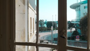 Vista a través de una ventana de un edificio con diseño arquitectónico moderno, que presenta una estructura cilíndrica destacada y un letrero con un círculo rojo y una línea que indica prohibido estacionar.