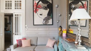Una sala de estar con un sofá gris, cojines decorativos, una chimenea con un espejo y una obra de arte enmarcada en la pared.