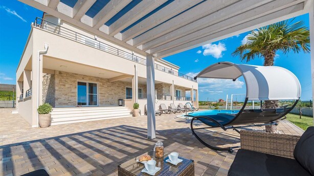 A covered outdoor area with a pool, lounge chairs, and a dining table. - Villa Providenca with heated pool (Debeljak)
