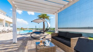 A covered outdoor area with a pool, lounge chairs, a wicker sofa, and a table with bread and drinks. - Villa Providenca with heated pool (Debeljak)