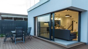 En moderne patio med spiseplads og en skydedør, der fører til et køkken med sofa og hængende lamper.