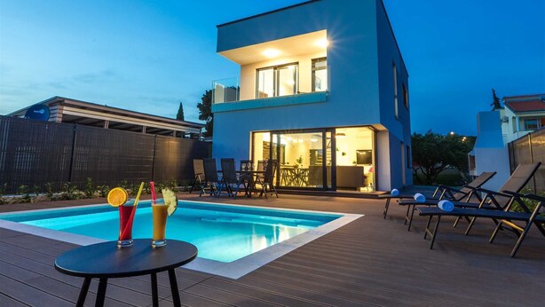 Et moderne hus i to etager med swimmingpool, udendørs siddepladser og et godt oplyst interiør.