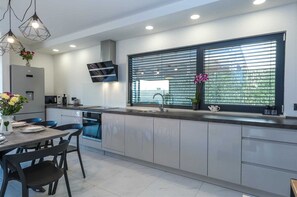 A modern kitchen with a built-in oven, a sink, and a window with blinds.
