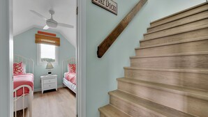A bedroom with two beds, a nightstand, a ceiling fan, and a wooden staircase. - In-town five bedroom townhouse - close to the beach! (Lewes)
