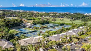 A residential area with multiple tennis courts, a swimming pool, and a view of the ocean.