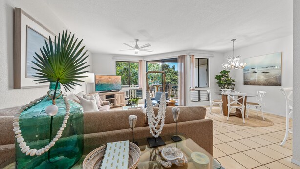 A modern living room with a glass coffee table, a green decorative bottle, and a large plant.