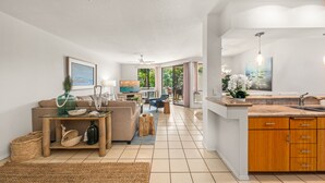 A spacious living area with a sofa, coffee table, and a dining table. There is a kitchen with wooden cabinets and a sink.
