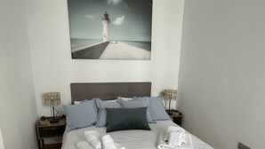Una cama bien hecha con sábanas y toallas blancas, un cabecero y un cuadro de un faro en la pared.