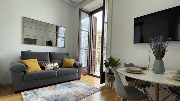 Una sala de estar moderna con un sofá gris, una mesa de centro y un comedor con una mesa y sillas blancas.