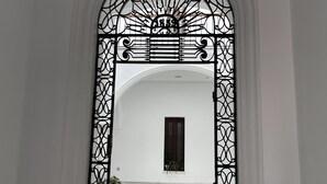 Una entrada arqueada con elaboradas puertas de hierro forjado y un pequeño ventanal con una puerta de madera oscura.