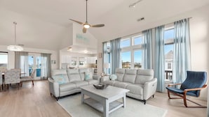 A spacious living room with a large sectional sofa, a coffee table, and a dining area with patterned chairs. - Blue Bomber: Oceanside | Pool/Hot Tub | Dogs OK (Corolla)
