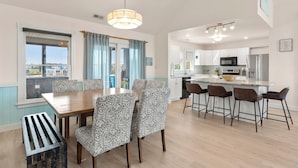 A modern kitchen with white cabinets, a central island, and bar stools. - Blue Bomber: Oceanside | Pool/Hot Tub | Dogs OK (Corolla)
