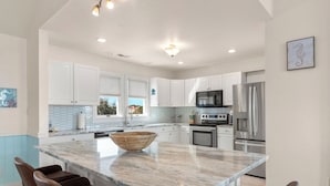 A modern kitchen with white cabinets, a marble island, and stainless steel appliances. - Blue Bomber: Oceanside | Pool/Hot Tub | Dogs OK (Corolla)