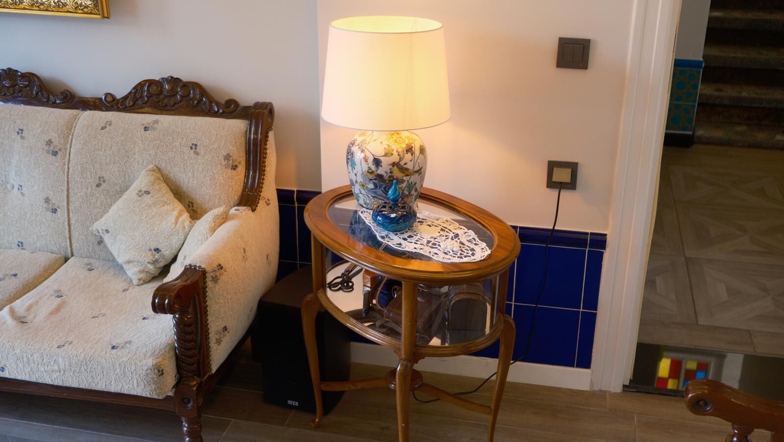 A room with a sofa, a table with a lamp, and a tiled wall.