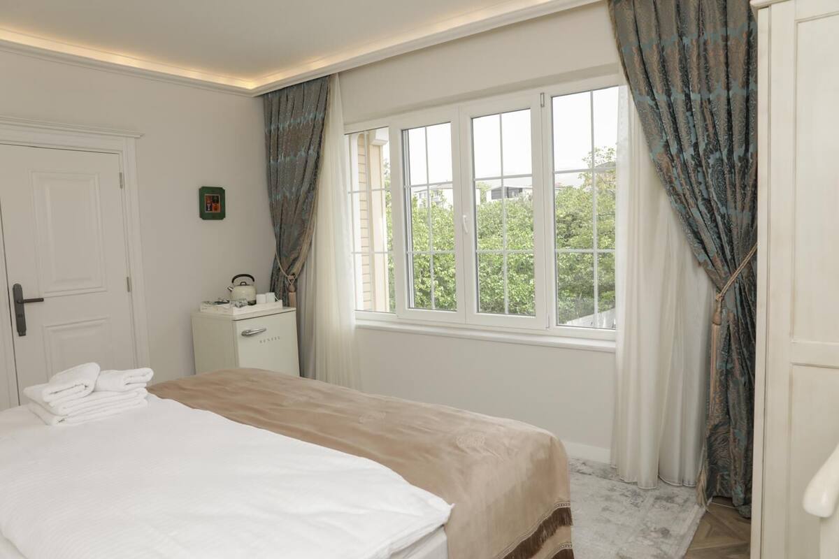 A bedroom with a bed, a bedside table, a window with curtains, and a door.