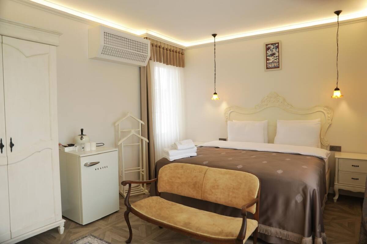 A hotel room with a bed, bedside tables, a wardrobe, a desk, and a chair.